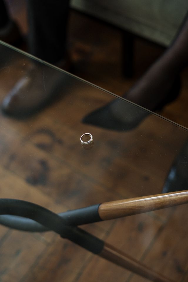 Alliance posée sur une table en verre au-dessus d'un parquet en bois, chaussures visibles en arrière-plan