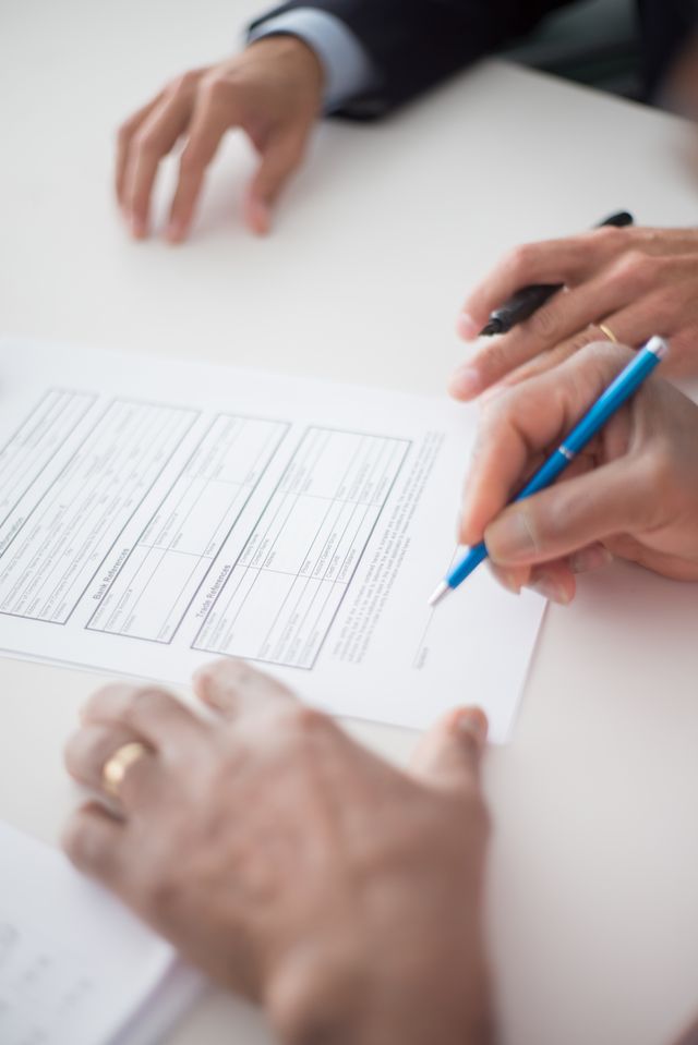Deux personnes en costume remplissant et signant ensemble un formulaire sur une table blanche