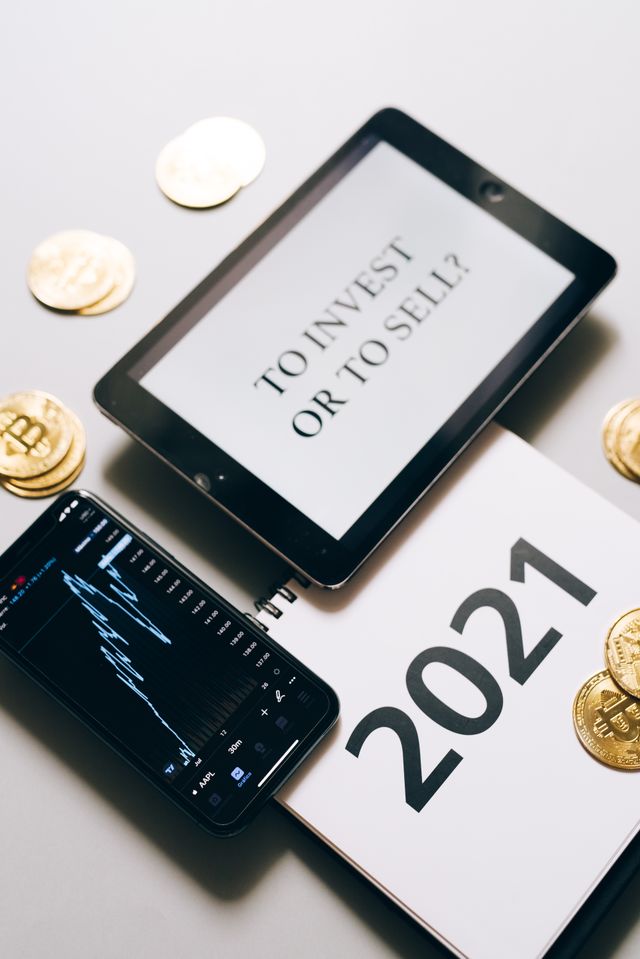 Tablette affichant To invest or to sell, smartphone avec graphique, pièces dorées et carnet 2021