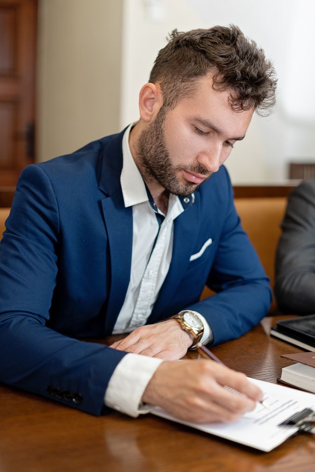 Homme barbu en veste bleue prenant des notes sur un document à un bureau en bois
