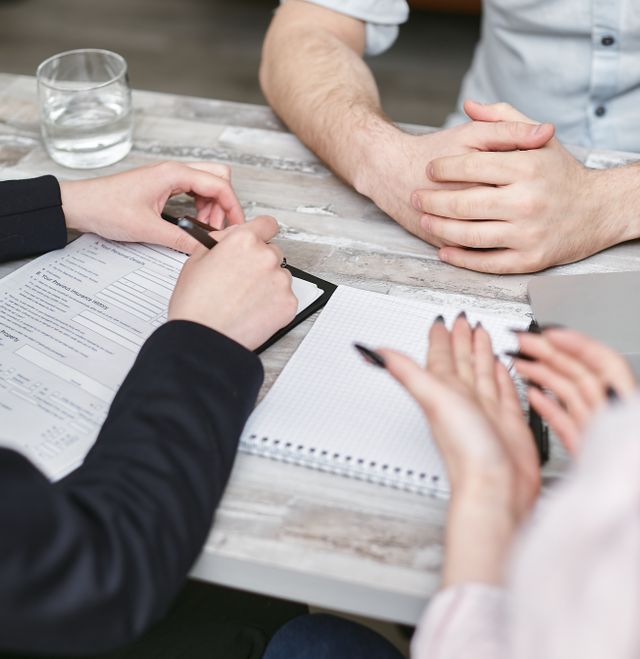 Trois personnes autour d'une table examinant un document et un carnet lors d'un rendez-vous de conseil