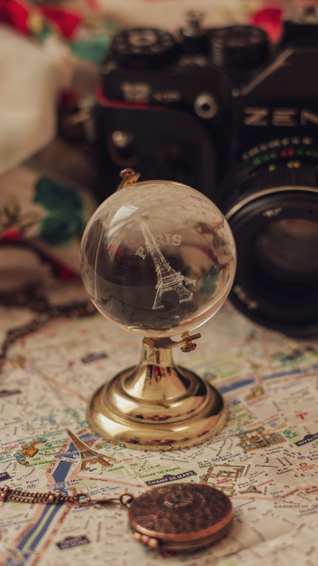 Globe terrestre en verre sur pied doré posé sur une carte, appareil photo argentique en arrière-plan