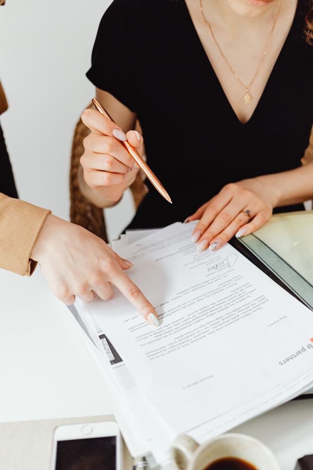 Deux femmes relisant un contrat, l'une désignant une ligne du doigt, l'autre tenant un crayon