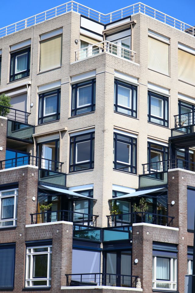 Immeuble résidentiel en briques beiges avec balcons et grandes fenêtres, vu en contre-plongée