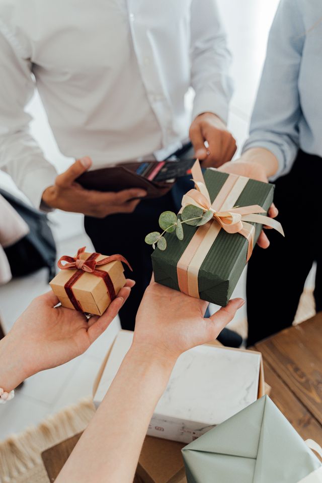 Mains échangeant des paquets cadeaux enrubannés autour d'une table, l'une tenant un portefeuille