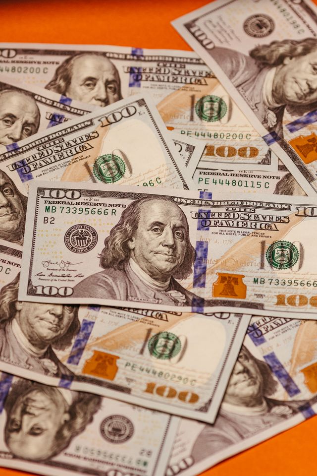 Billets de 100 dollars américains étalés en vrac sur une surface orange, vus en gros plan