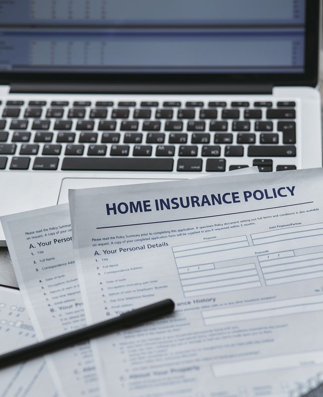 Formulaires Home Insurance Policy posés sur le clavier d'un ordinateur portable avec un stylo