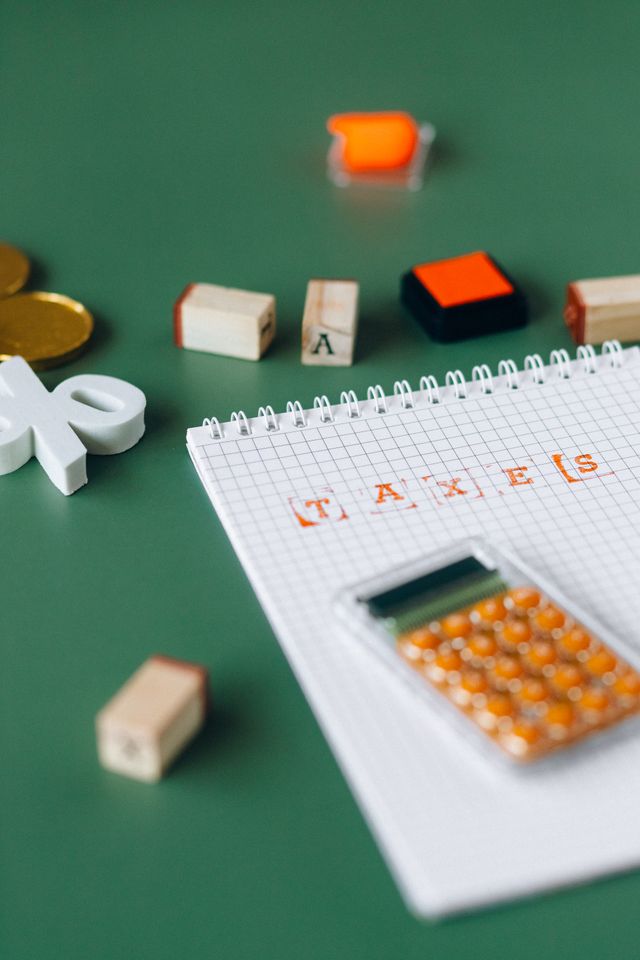 Bloc-notes quadrillé portant le mot Taxes, calculatrice orange et cubes en bois sur fond vert
