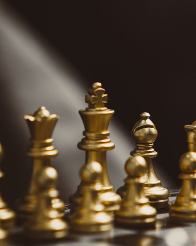 Pièces d'échecs dorées alignées sur un échiquier, roi et dame au premier plan, fond sombre