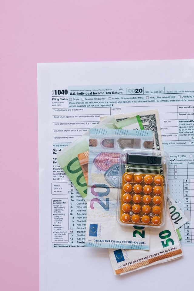 Billets en euros, calculatrice orange et formulaire de déclaration d'impôt posés sur fond rose