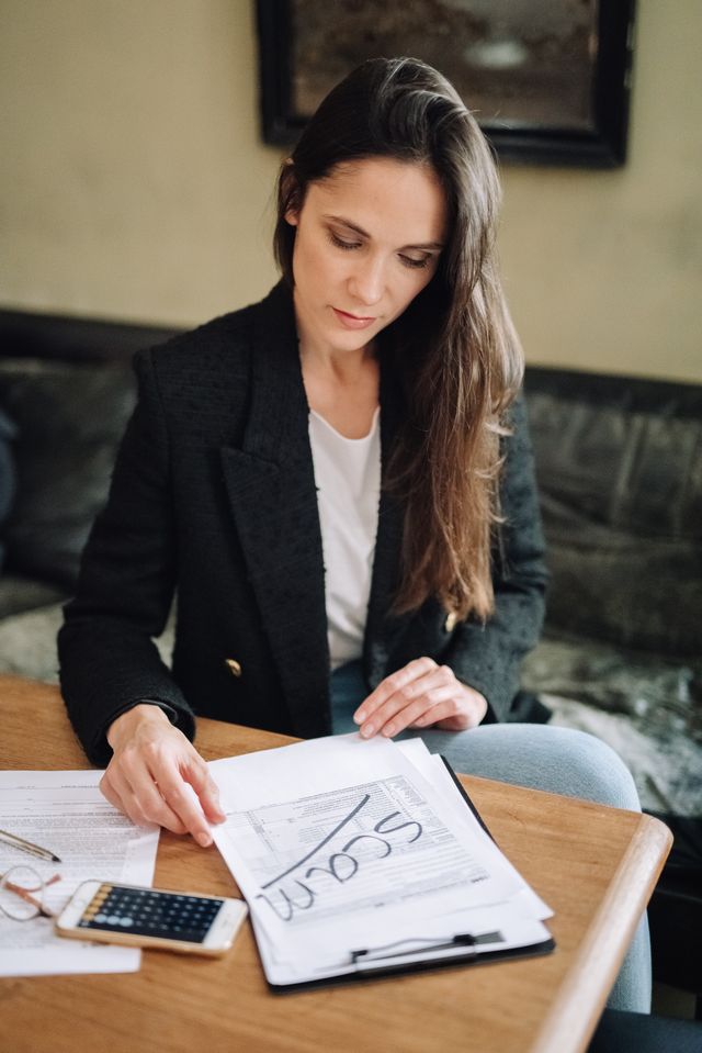 Femme aux cheveux longs relisant des documents à une table avec calculatrice et téléphone