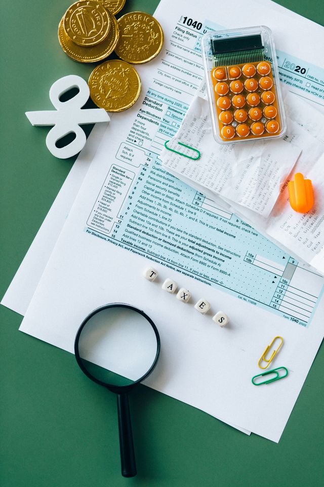 Formulaires fiscaux, calculatrice, loupe, pièces dorées et cubes formant le mot Taxes sur fond vert