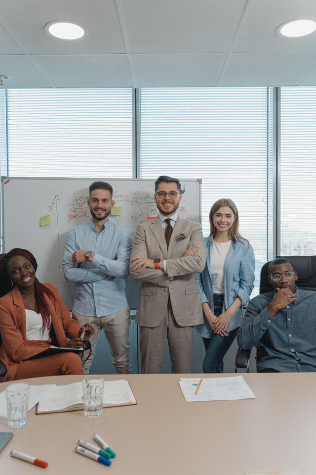 Équipe de six collègues souriants réunis autour d'une table de réunion devant un tableau blanc