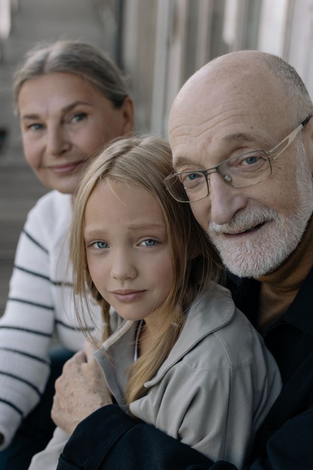 Grands-parents souriants serrant contre eux leur petite-fille blonde dans un intérieur
