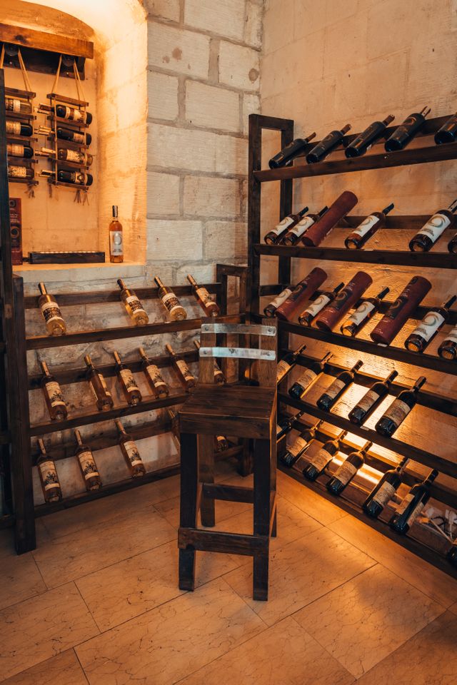 Cave à vin voûtée en pierre avec casiers en bois remplis de bouteilles et tabouret au centre