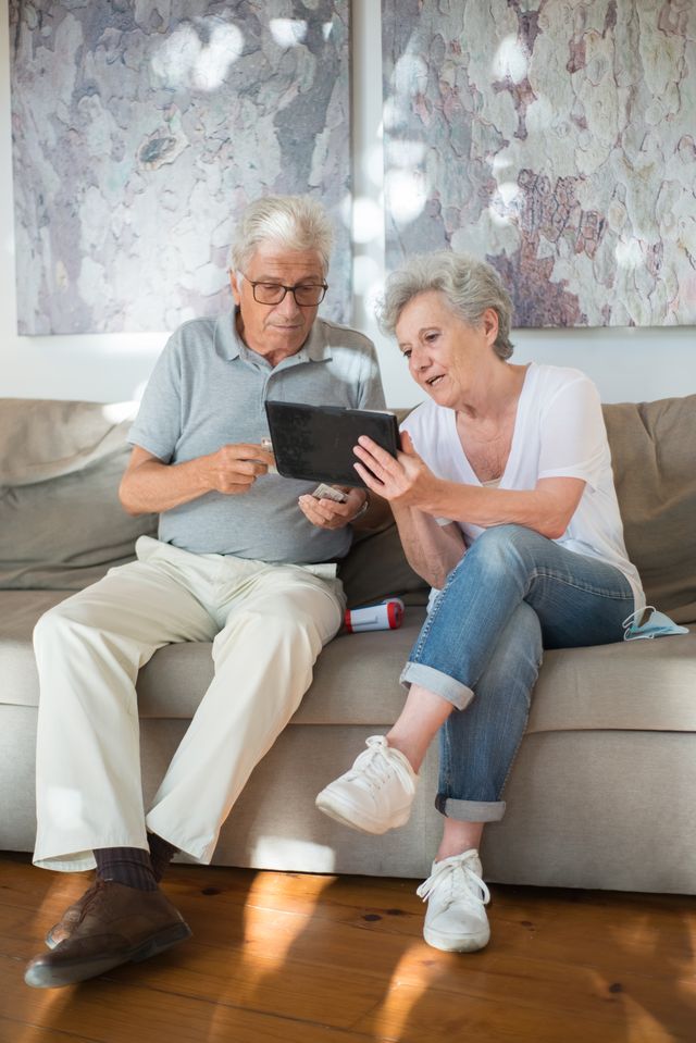 Couple de seniors souriants consultant une tablette, assis sur un canapé dans leur salon