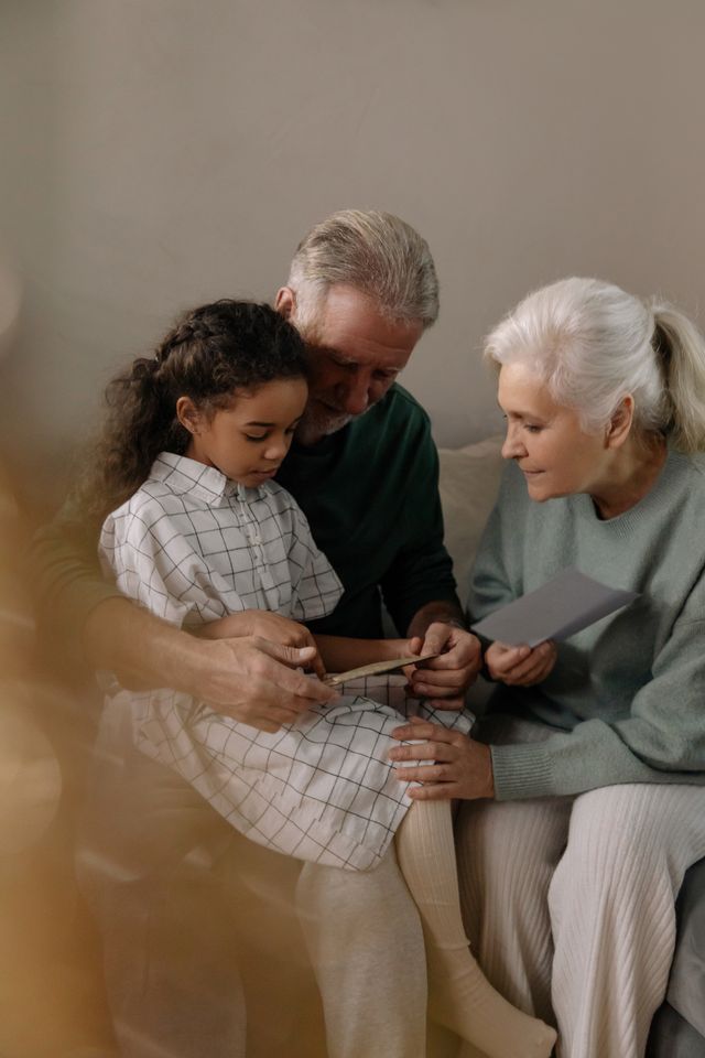Grand-père tenant sa petite-fille sur ses genoux, à côté de la grand-mère, sur un canapé