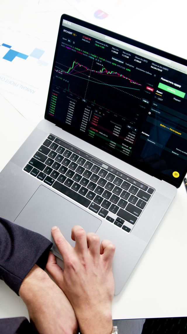 Mains d'une personne devant un ordinateur portable affichant une plateforme de trading