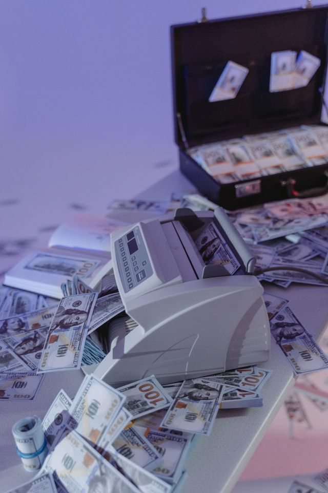 Compteuse de billets entourée de liasses de dollars éparpillées et d'une mallette ouverte remplie d'argent