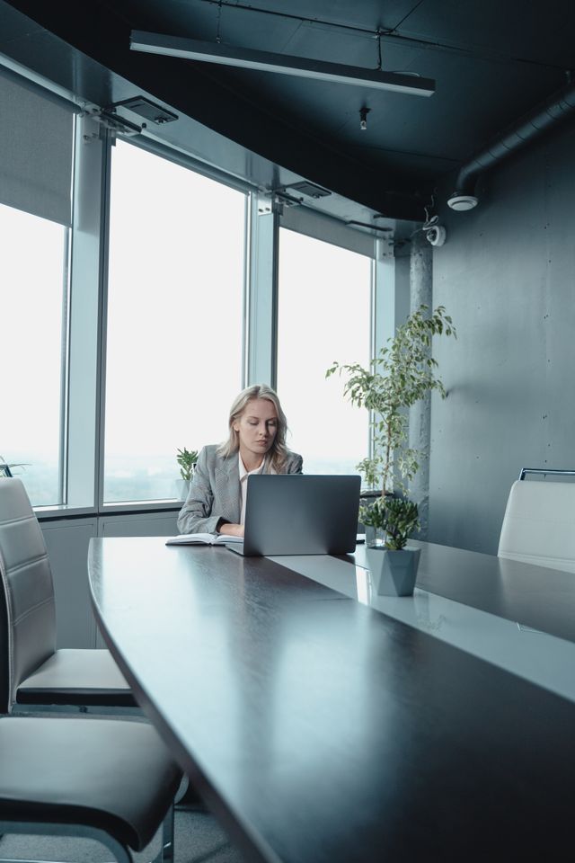 Femme travaillant seule sur un ordinateur portable au bout d'une longue table de réunion vitrée