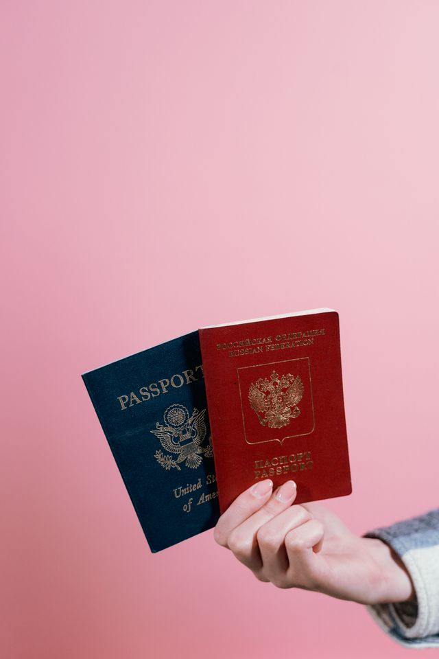 Main tenant un passeport américain bleu et un passeport russe rouge devant un fond rose