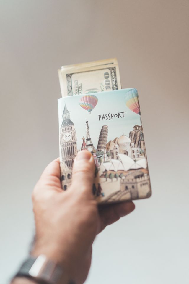 Main tenant un étui de passeport illustré de monuments, avec des billets de dollars glissés à l'intérieur