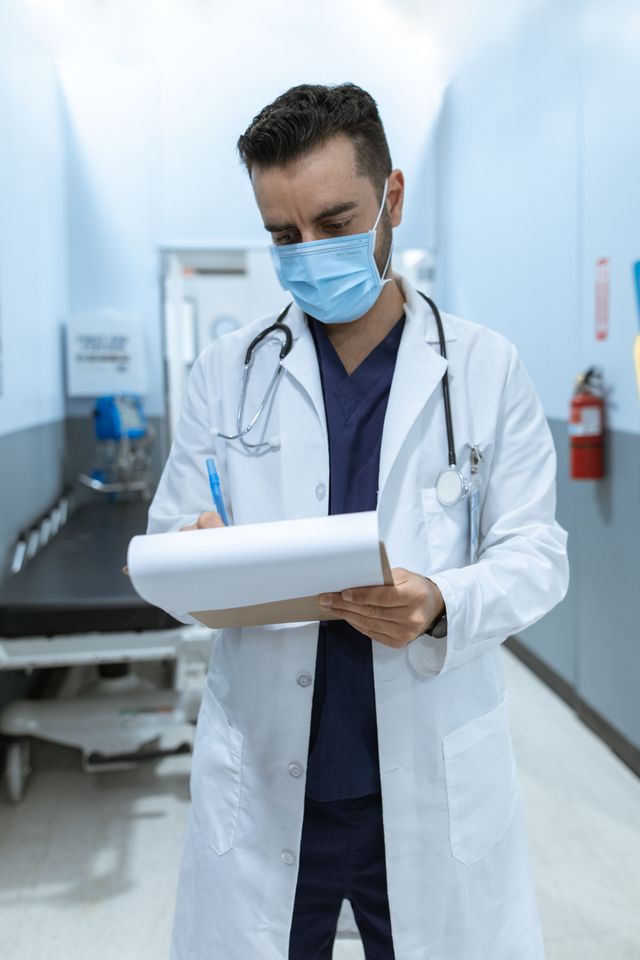 Médecin masqué en blouse blanche consultant un dossier dans un couloir d'hôpital
