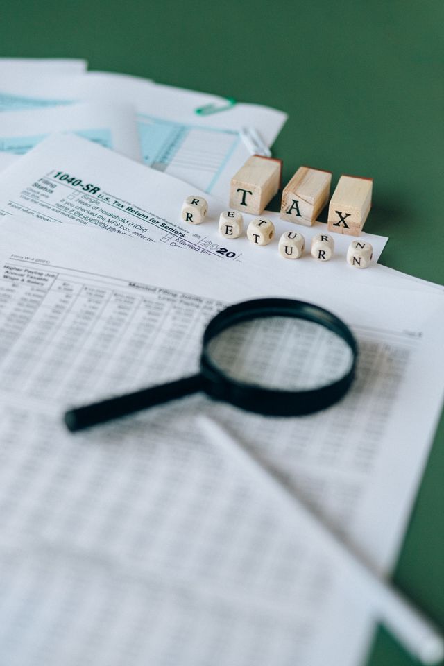 Loupe posée sur des tableaux fiscaux imprimés, cubes en bois formant les mots Tax return