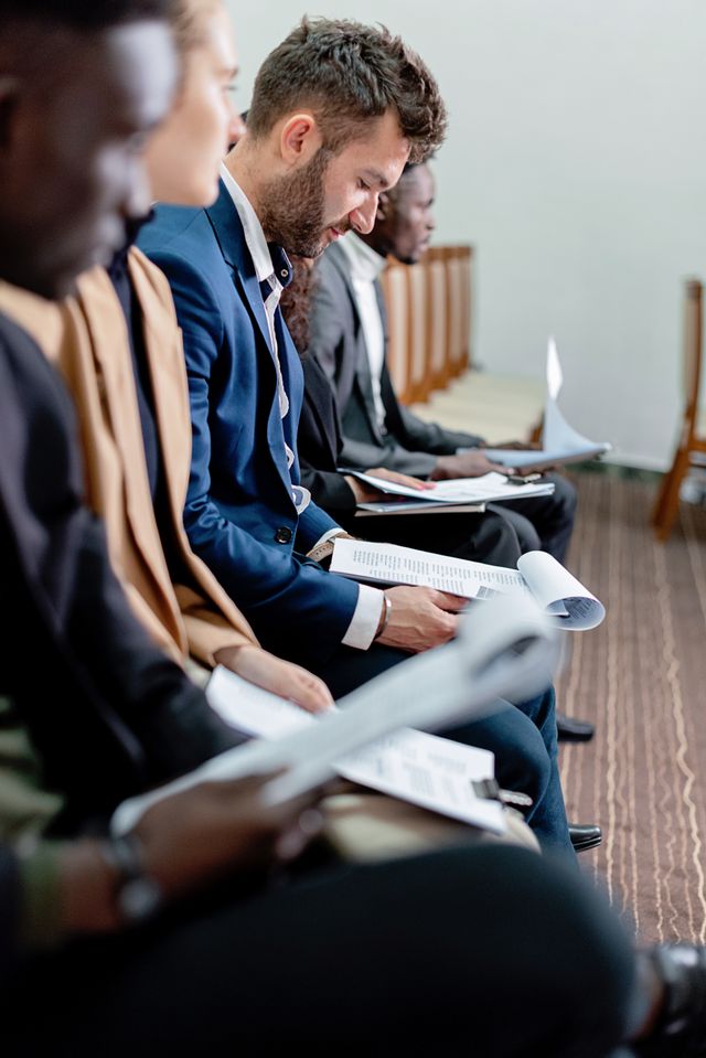 Rangée de personnes en tenue de bureau assises, consultant des documents en attendant leur tour