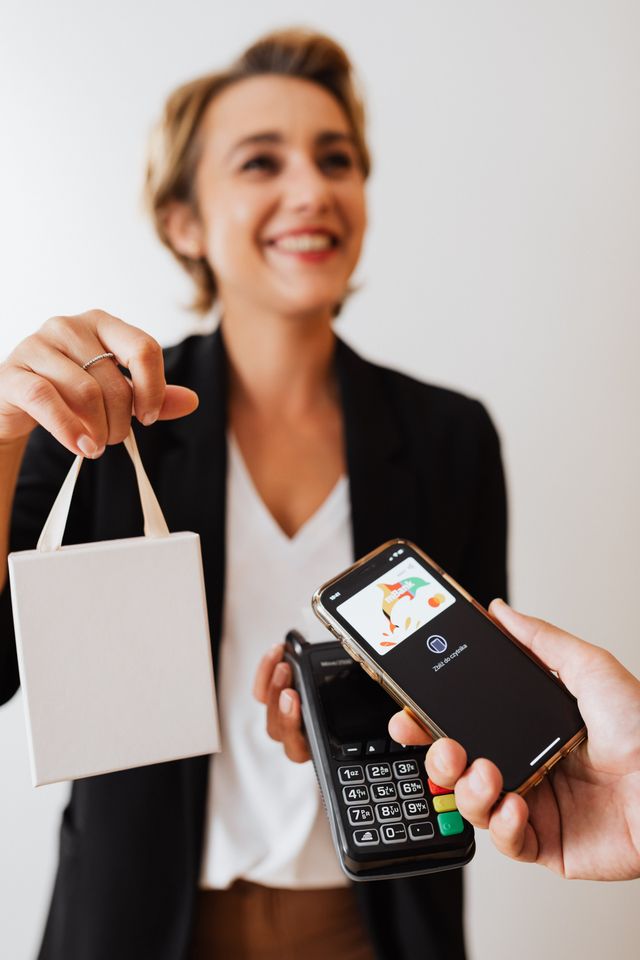 Femme souriante tendant un sac cadeau pendant qu'un client paie par smartphone sur un terminal