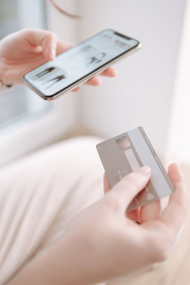 Mains tenant un smartphone affichant une boutique en ligne et une carte bancaire