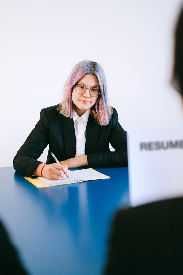 Jeune femme aux cheveux roses en blazer remplissant un document face à un recruteur