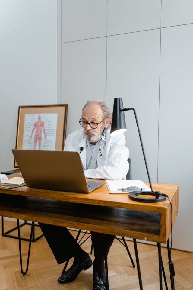 Médecin âgé travaillant sur un ordinateur portable dans un cabinet moderne avec planche anatomique