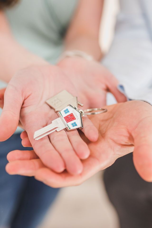 Mains ouvertes l'une dans l'autre tenant une clé accrochée à un porte-clé en forme de maison
