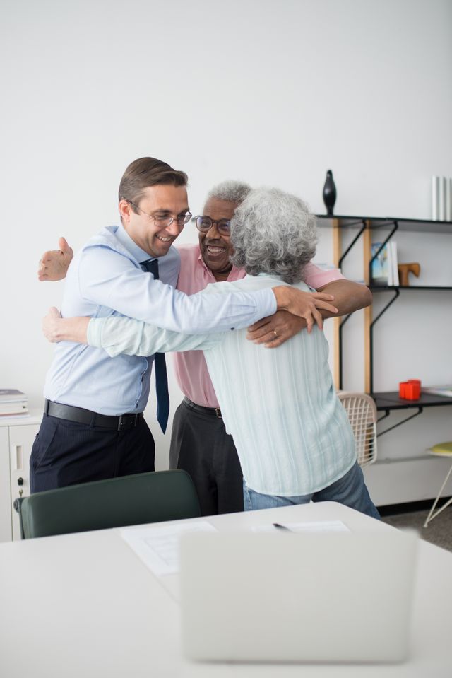Couple de seniors serrant chaleureusement dans ses bras un conseiller en chemise et cravate