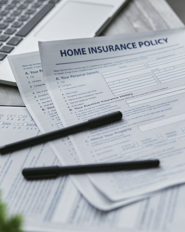 Formulaires d'assurance habitation posés près d'un ordinateur avec deux stylos noirs