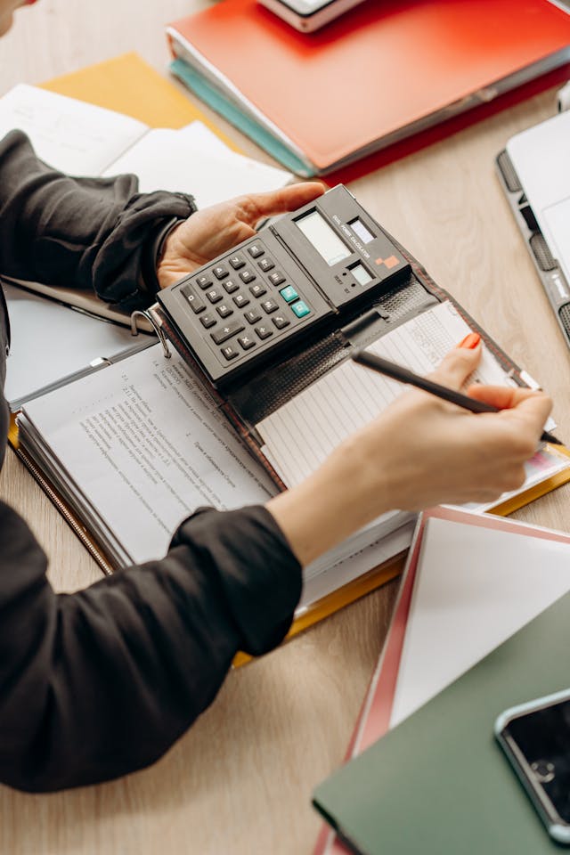 Mains utilisant une calculatrice et un crayon sur des documents classés dans un porte-bloc
