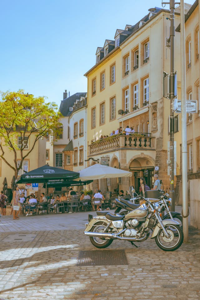 Place pavée du centre de Luxembourg avec terrasses de café, moto garée et façades claires