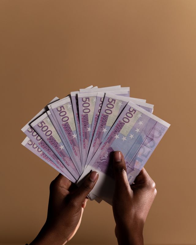 Mains tenant en éventail une épaisse liasse de billets de 500 euros sur fond marron uni