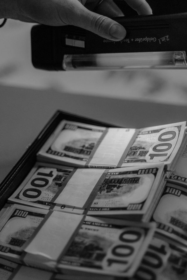Photo en noir et blanc de liasses de billets de 100 dollars sous une lampe de contrôle