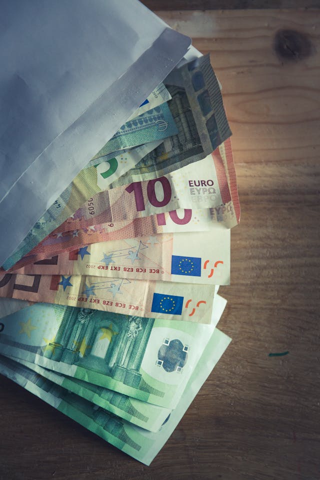 Billets de 50, 20 et 10 euros dépassant d'une enveloppe posée sur une table en bois