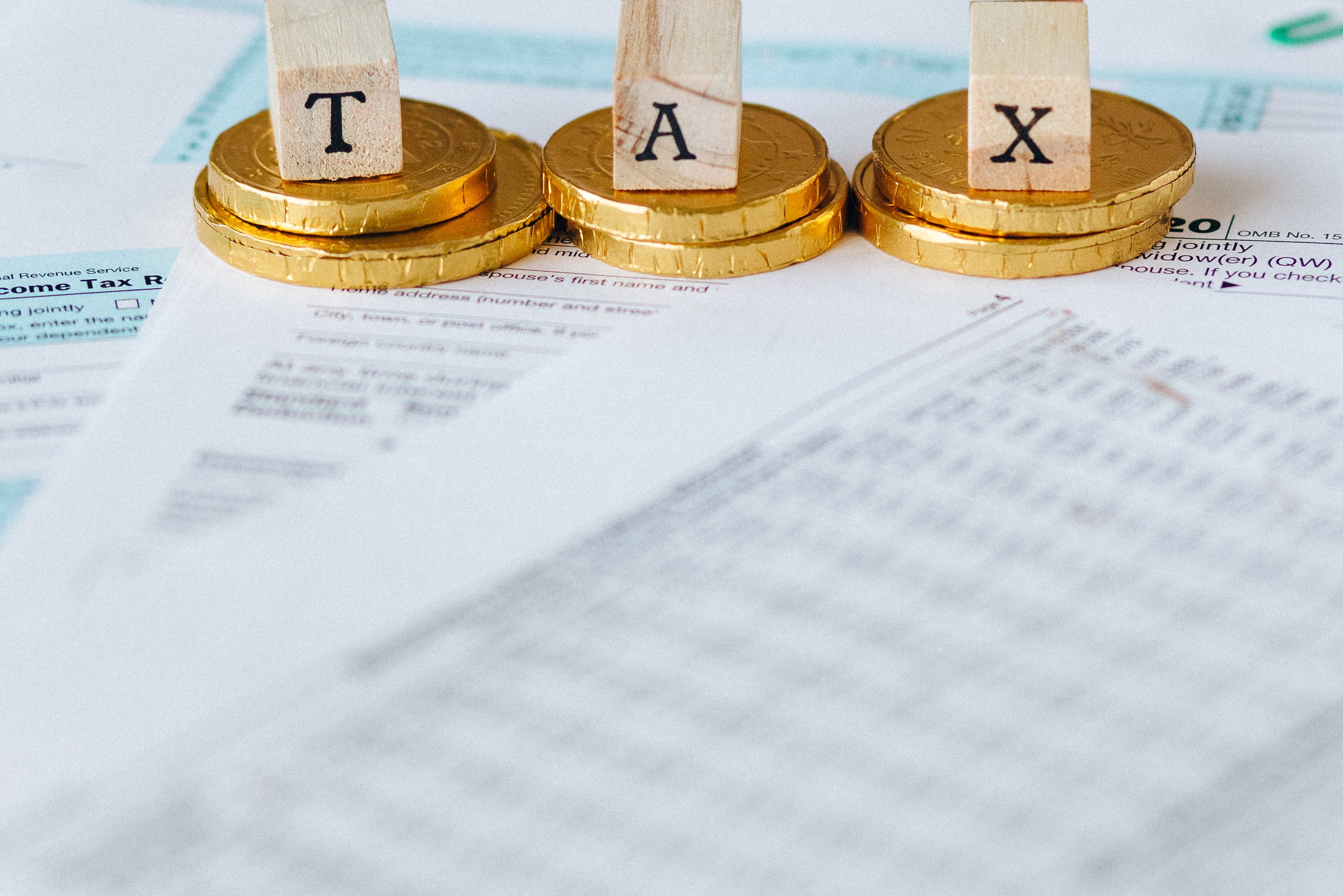 Cubes en bois formant le mot Tax posés sur des piles de pièces dorées, formulaires flous
