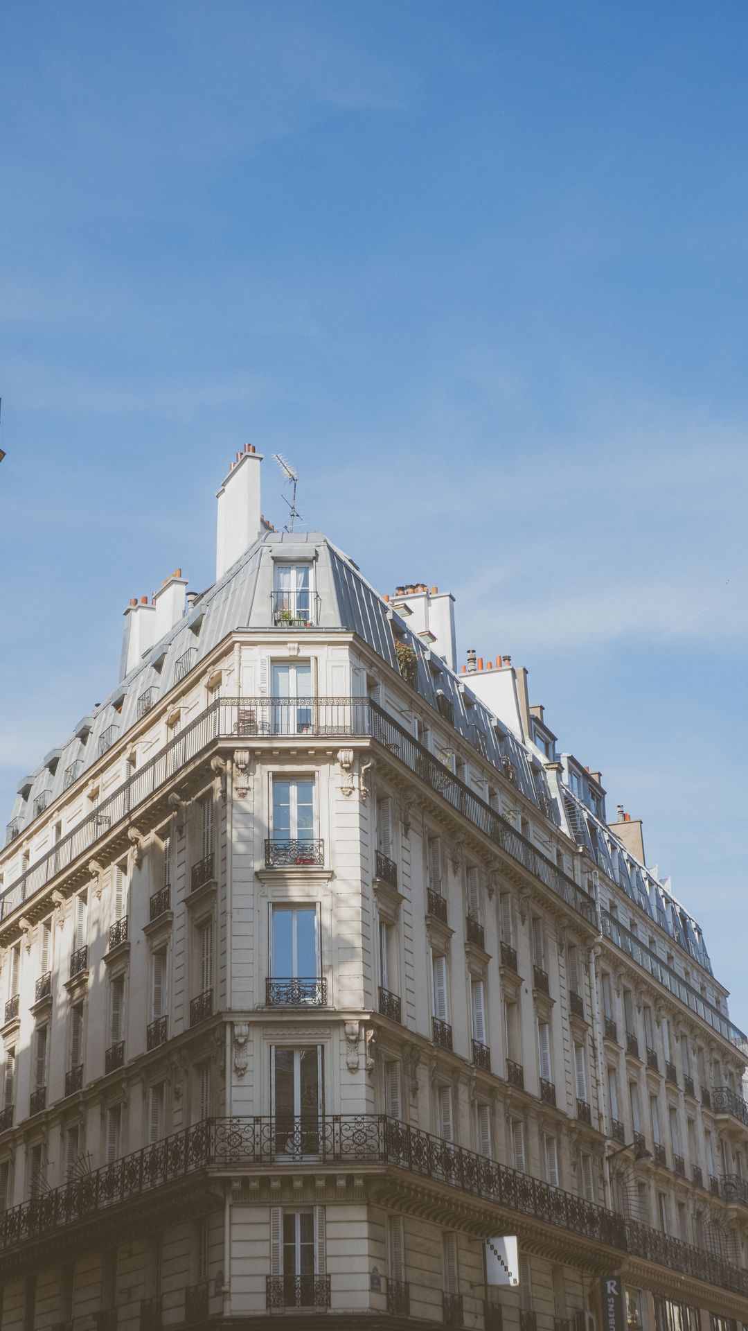 Immeuble haussmannien d'angle à Paris, façade en pierre claire et balcons en fer forgé, sous un ciel bleu dégagé