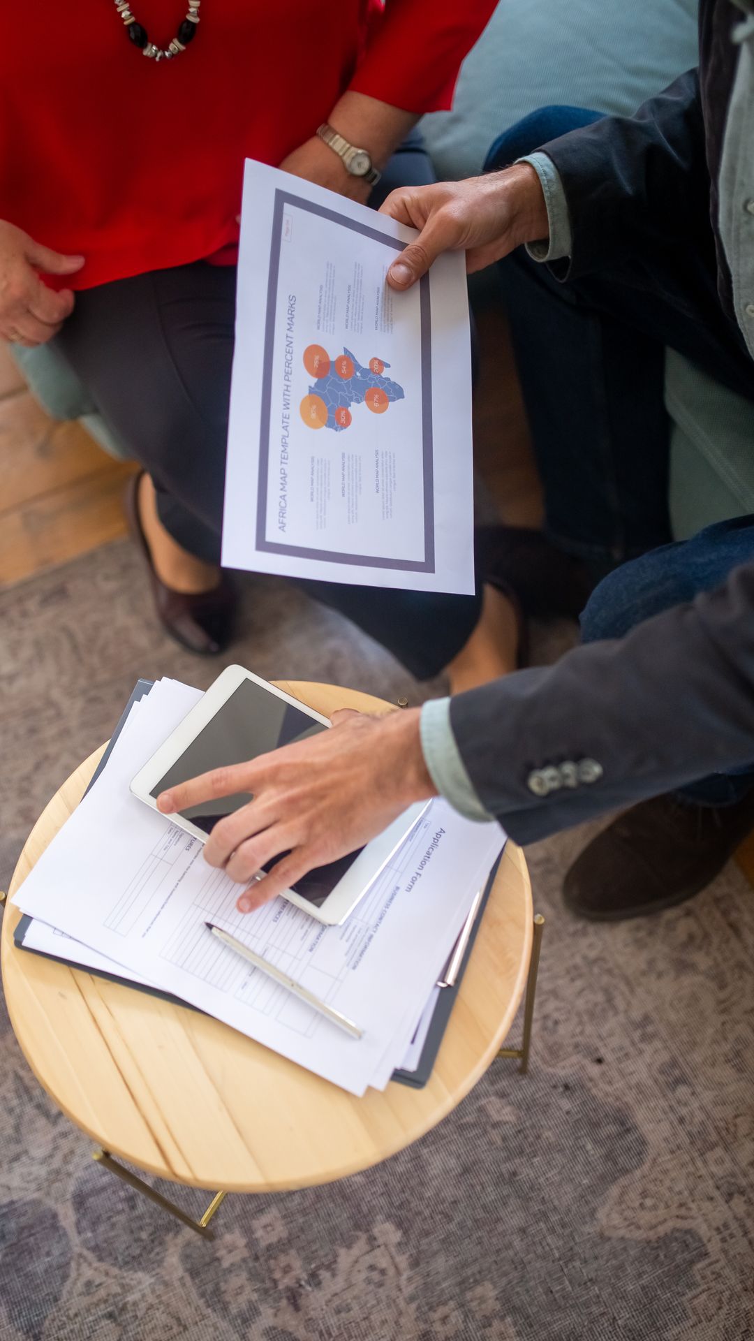 Mains tenant un document illustré au-dessus d'une table basse ronde où reposent une tablette et des papiers