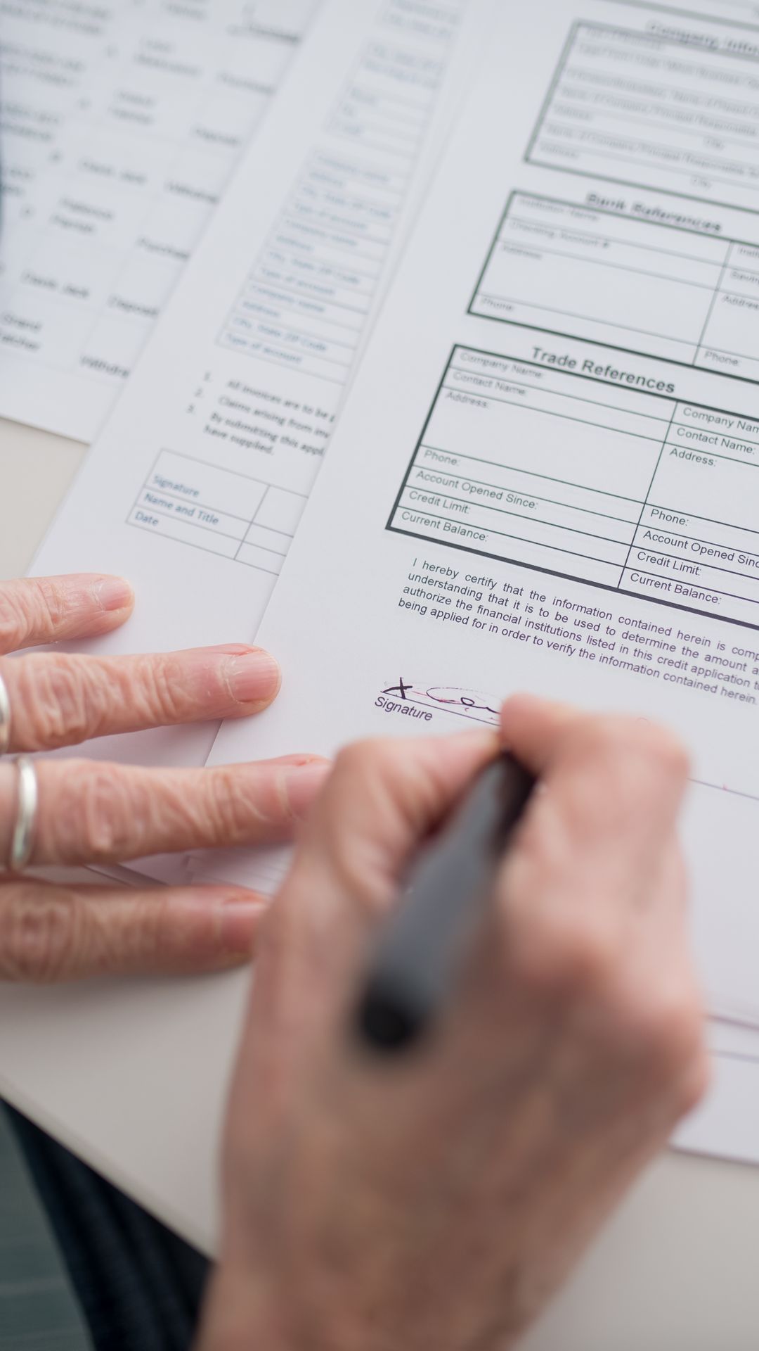 Main d'une personne âgée signant un formulaire imprimé au stylo, l'autre main posée à plat sur la feuille