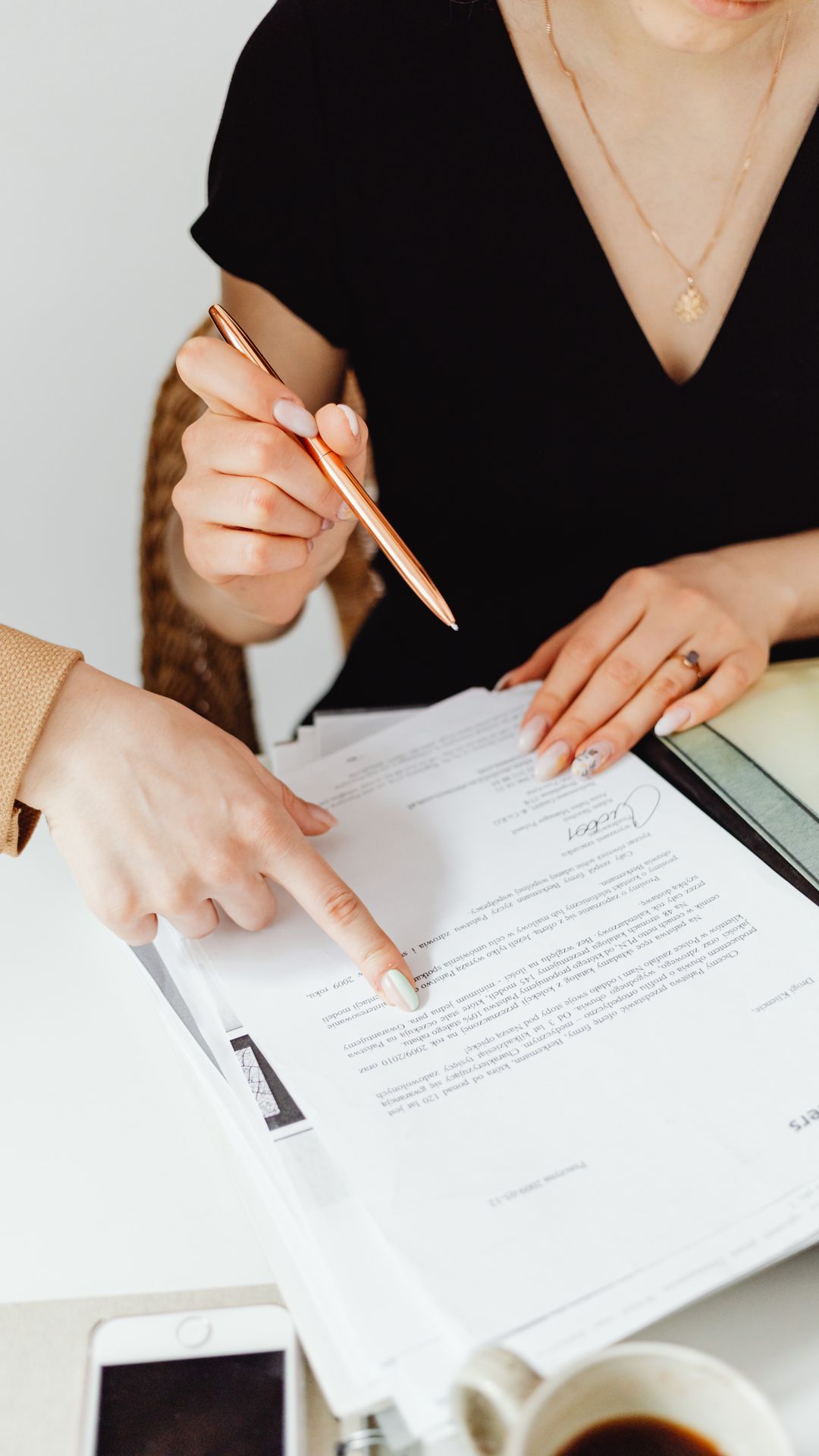 Femme en robe noire tenant un stylo doré pendant qu'une autre main désigne une ligne d'un document imprimé
