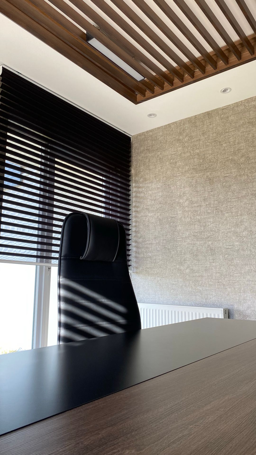 Bureau de direction inoccupé avec fauteuil en cuir noir, stores fermés et plafond à lattes de bois