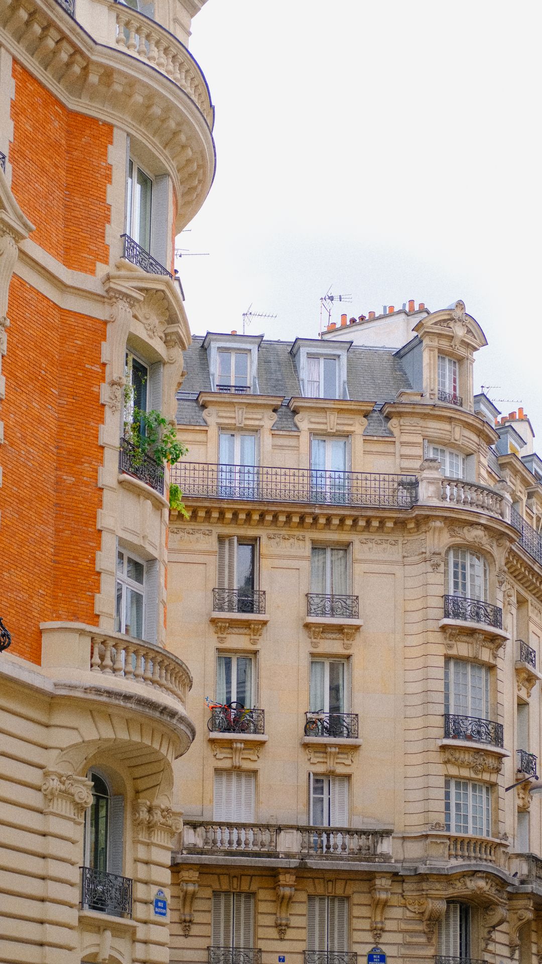 Façade d'immeubles parisiens en pierre de taille et brique, avec balcons en fer forgé et toits en zinc