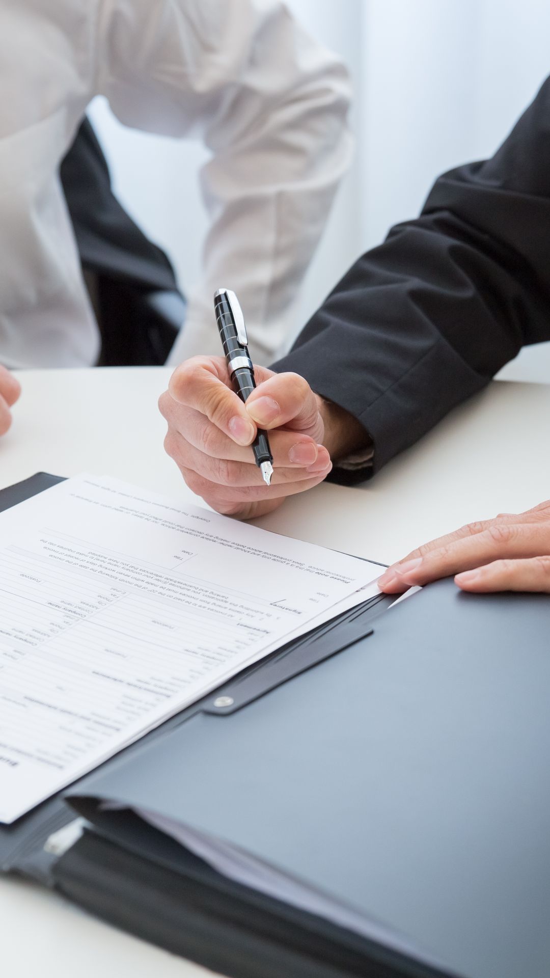 Main tenant un stylo plume au-dessus d'un contrat posé sur une table, lors d'une signature