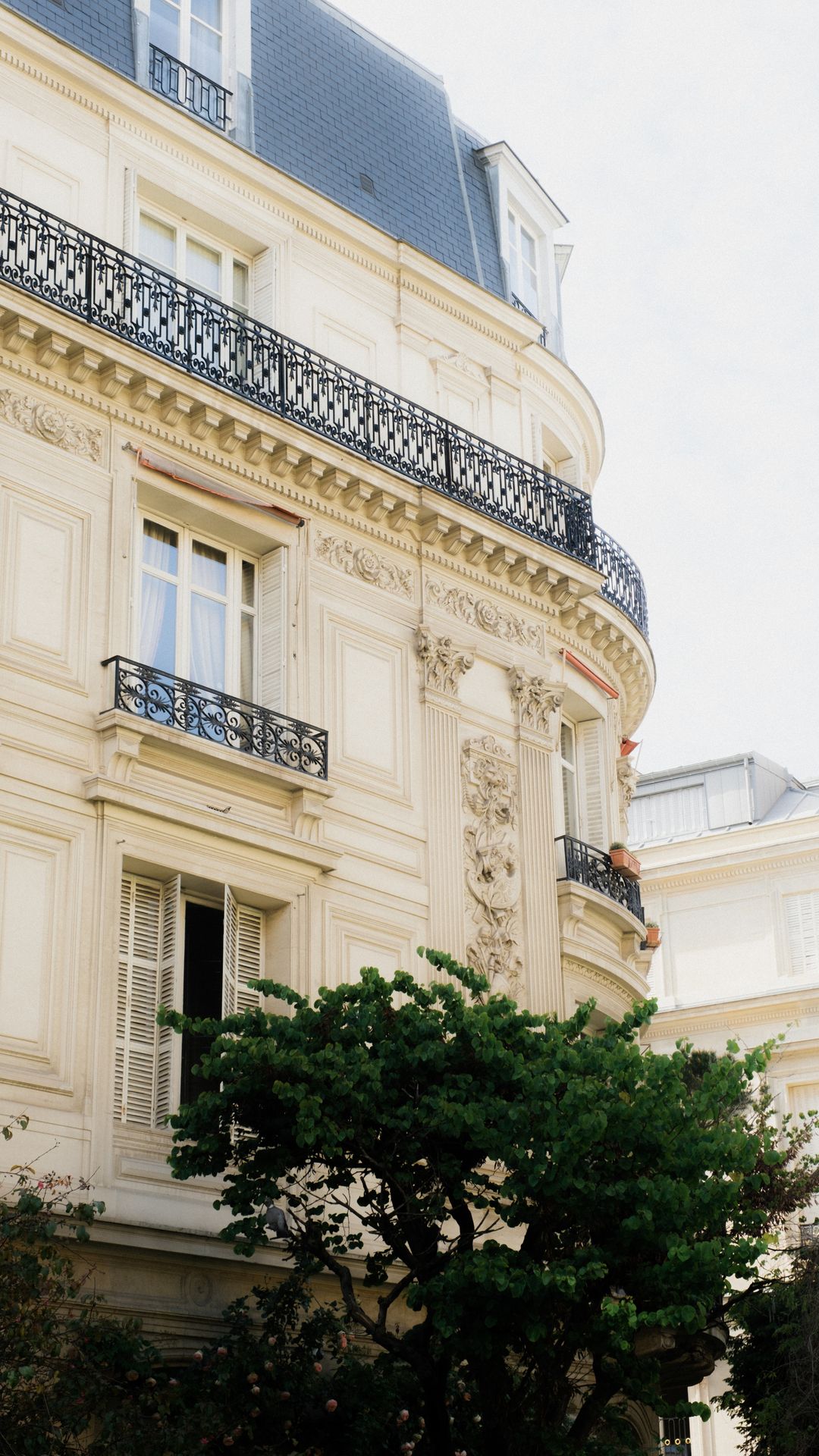 Façade d'un immeuble parisien clair avec balcons en fer forgé, volets et toit en zinc